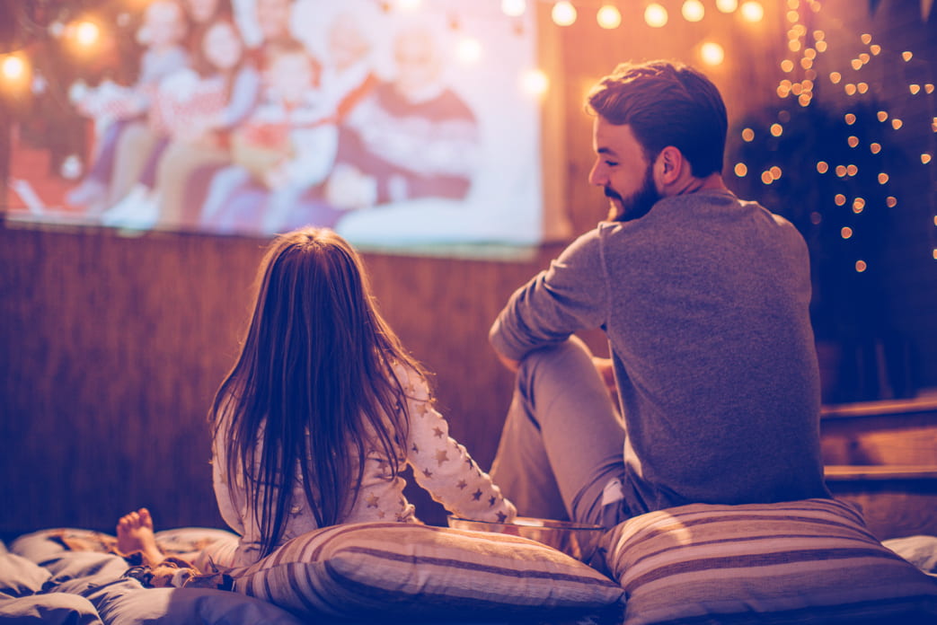An image of a father and daughter facing an outdoor movie screen