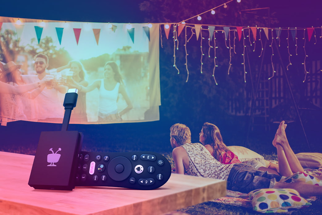 An image of the TiVo Stream 4k and remote with a couple in the background watching a movie outdoors
